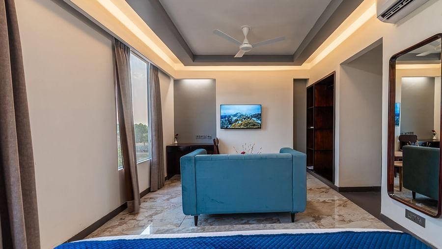 Deluxe King Room's living area with a plush blue sofa and stylish decor at Clarks Inn Suites Jaipur, Ajmer Road